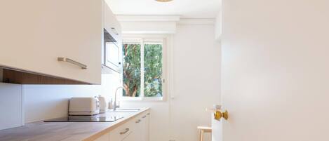 A modern kitchen with a wooden countertop, built-in appliances, and a window providing a view of greenery.