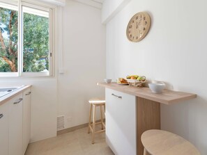 Eine Küche mit Fenster, einer Holz-Uhr, einem Obstkorb und einem Hocker.