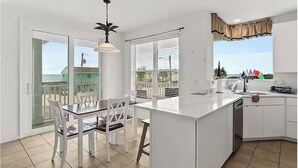 A modern kitchen with a central island, white cabinetry, and a dining area with a table and chairs. - 4-Bedroom Villa in Flagler Beach with priority beach access (Flagler Beach)