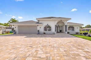 A modern two-story house with a large driveway, garage, and arched windows. - WATERFRONT - Walk to Beach, Pool/Spa, Kayaks, Bikes, Direct Gulf Access - Retro Retreat - Roelens (Cape Coral)