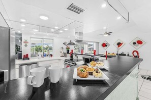 A modern kitchen with a black countertop, white appliances, and a dining area with a table set for a meal. - WATERFRONT - Walk to Beach, Pool/Spa, Kayaks, Bikes, Direct Gulf Access - Retro Retreat - Roelens (Cape Coral)