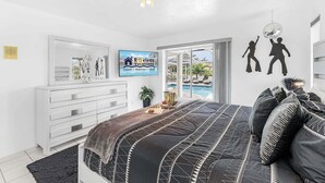 Quarto moderno com cama, penteadeira, TV e vista para uma piscina.