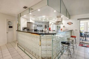 A modern kitchen with a glass island, stainless steel appliances, and a bicycle decoration on the wall. - WATERFRONT - Walk to Beach, Pool/Spa, Kayaks, Bikes, Direct Gulf Access - Retro Retreat - Roelens (Cape Coral)