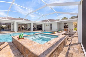 A pool area with a hot tub, lounge chairs, and a covered patio. - WATERFRONT - Walk to Beach, Pool/Spa, Kayaks, Bikes, Direct Gulf Access - Retro Retreat - Roelens (Cape Coral)