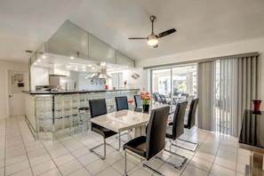 A modern kitchen with a central island, dining area with chairs, and a ceiling fan. - WATERFRONT - Walk to Beach, Pool/Spa, Kayaks, Bikes, Direct Gulf Access - Retro Retreat - Roelens (Cape Coral)