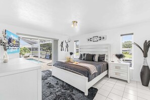 A bedroom with a bed, bedside table, and a view of the outdoors. - WATERFRONT - Walk to Beach, Pool/Spa, Kayaks, Bikes, Direct Gulf Access - Retro Retreat - Roelens (Cape Coral)