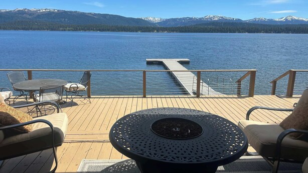 Una terraza con mobiliario exterior, una fogata y vistas a un lago con montañas al fondo.