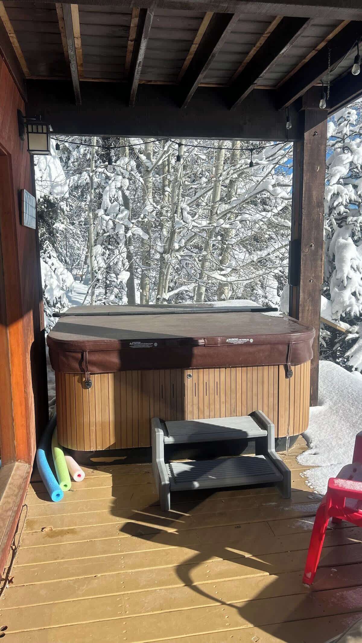 A hot tub with a wooden deck and a view of snow-covered trees.