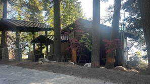 Un chalet rustique à la structure en bois et aux murs en pierre, entouré d’arbres et bordé d’un chemin pavé.