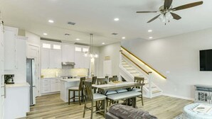 A modern kitchen with white cabinets, a dining area with a wooden table and chairs, a leather sofa, and a staircase with a light fixture. - Spacious 4-bedroom house, with boat parking!!!Close to a boat ramp (Rockport)