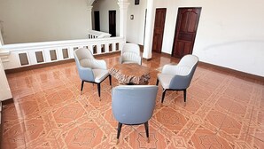 Un vestíbulo amplio con suelo estampado, columnas blancas y una zona de estar con sillas y una mesa redonda.