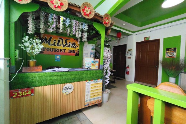 A reception desk with a sign for 'Milvis Tourist Inn', a business registration permit, and a welcome sign.