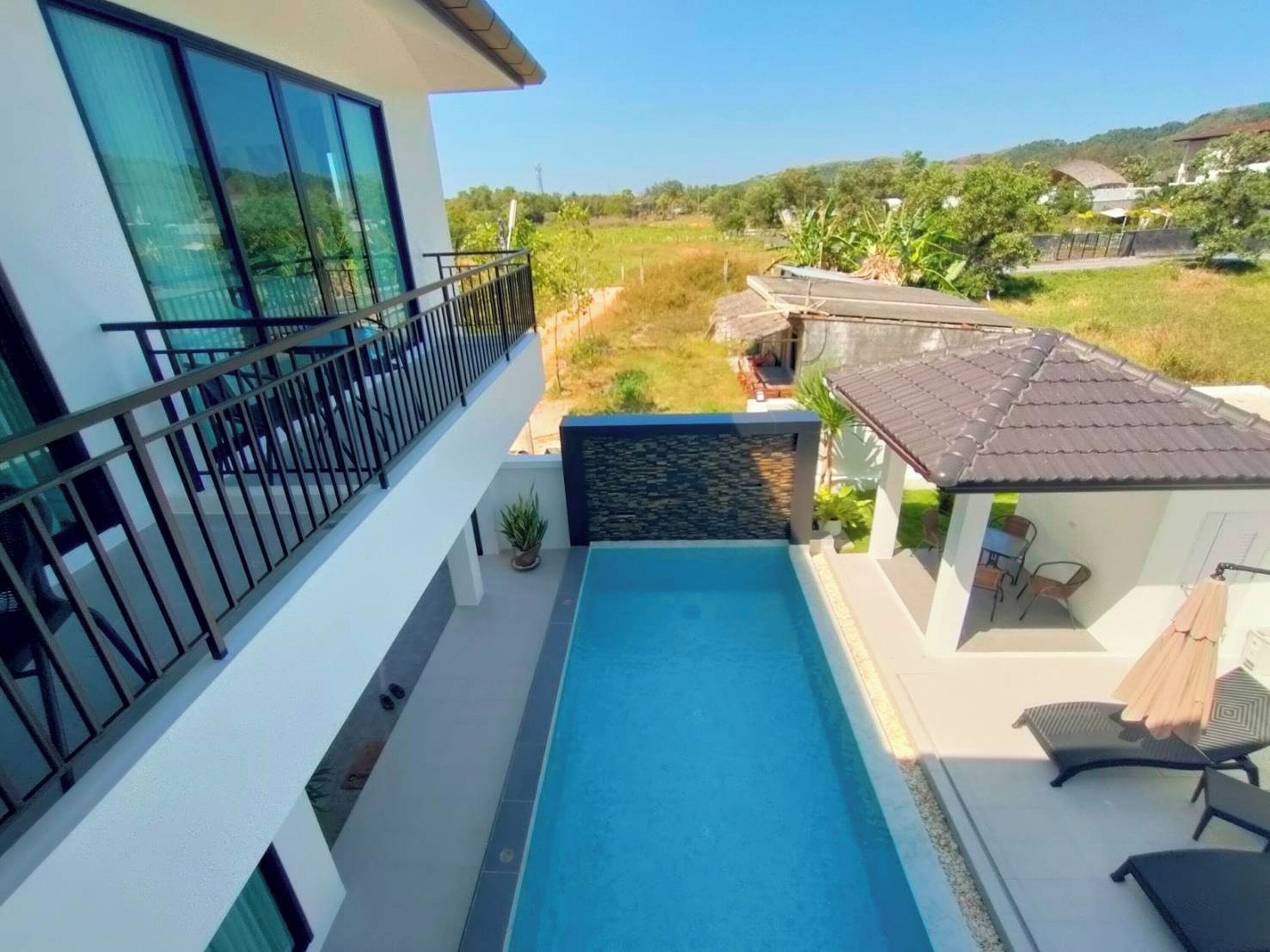 A modern building with a rooftop pool, a balcony with a railing, and a view of the surrounding landscape.