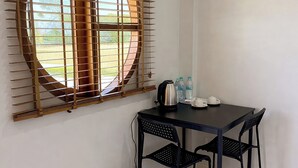 A small room with a table and two chairs, a window with blinds, a kettle, and two water bottles. - The 9 Motel (Ngao)