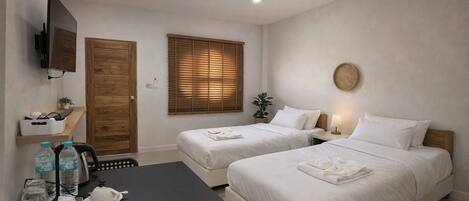 A hotel room with two beds, a TV mounted on the wall, a wooden door, and a window with blinds.