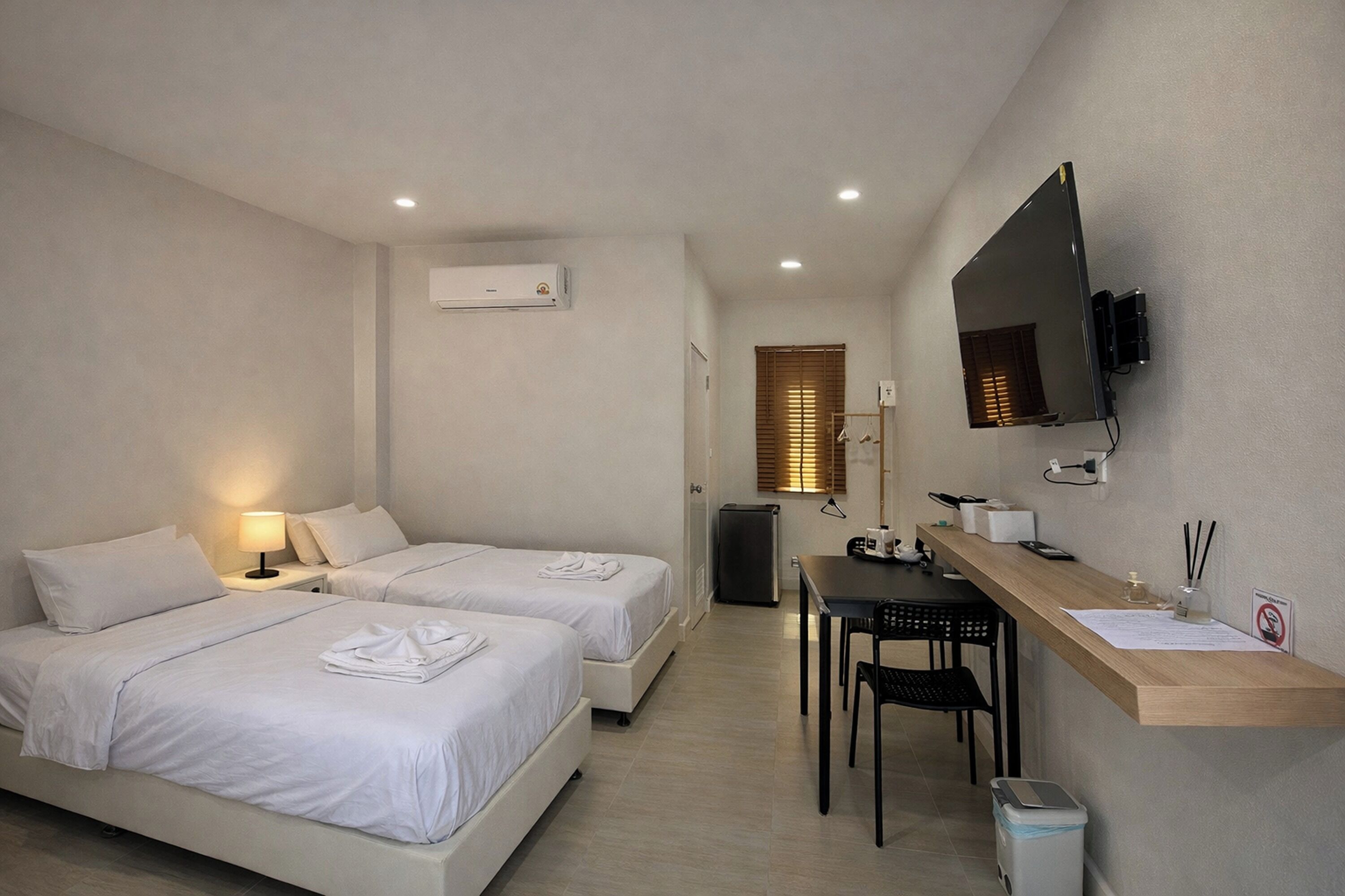 A hotel room with two beds, a desk, a chair, a TV, and a trash bin.