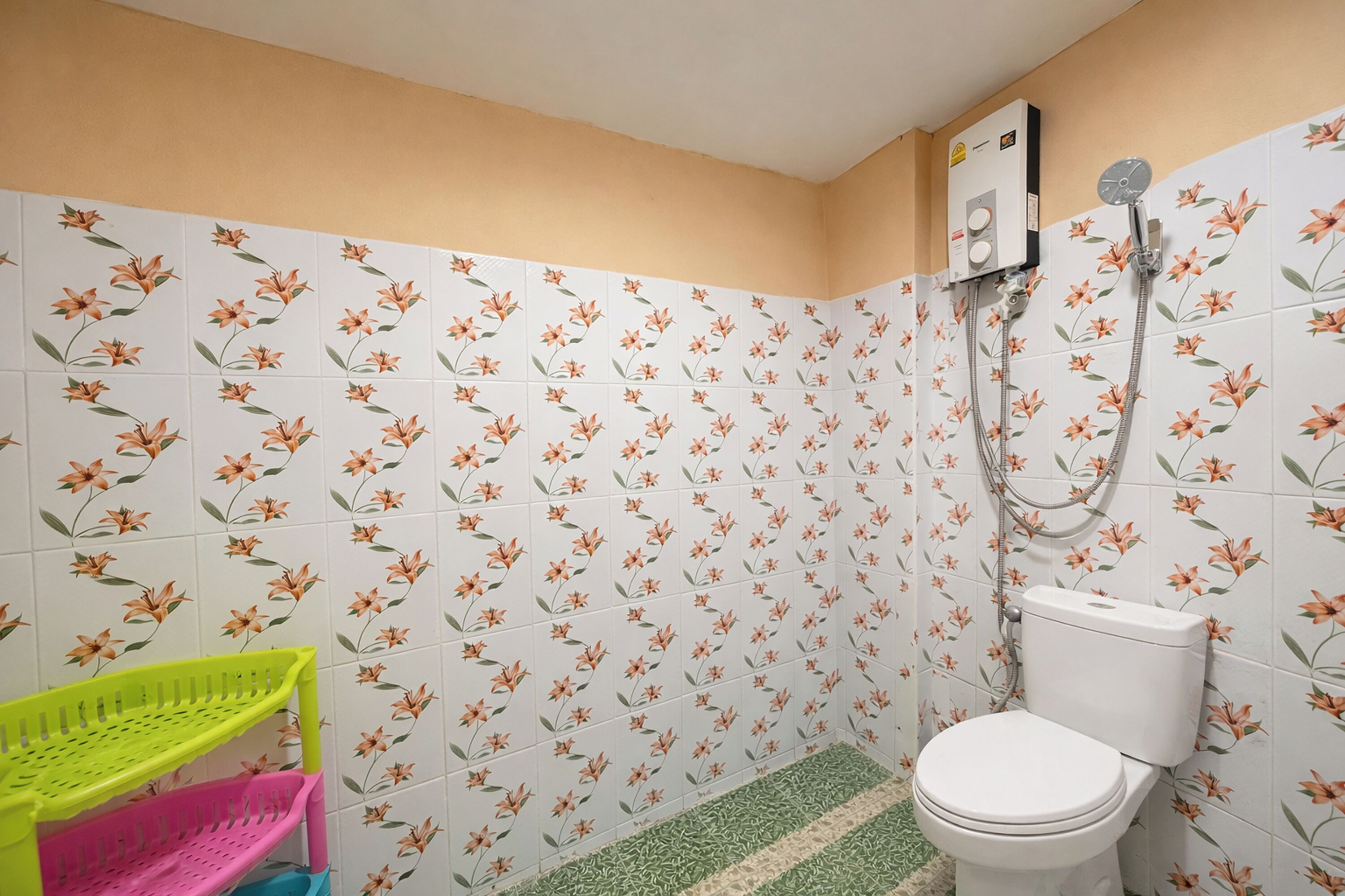 Un baño con azulejos de motivos florales, un inodoro blanco y una ducha.