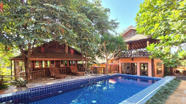 A pool area with a tiled blue pool, wooden deck, and a building with a balcony.