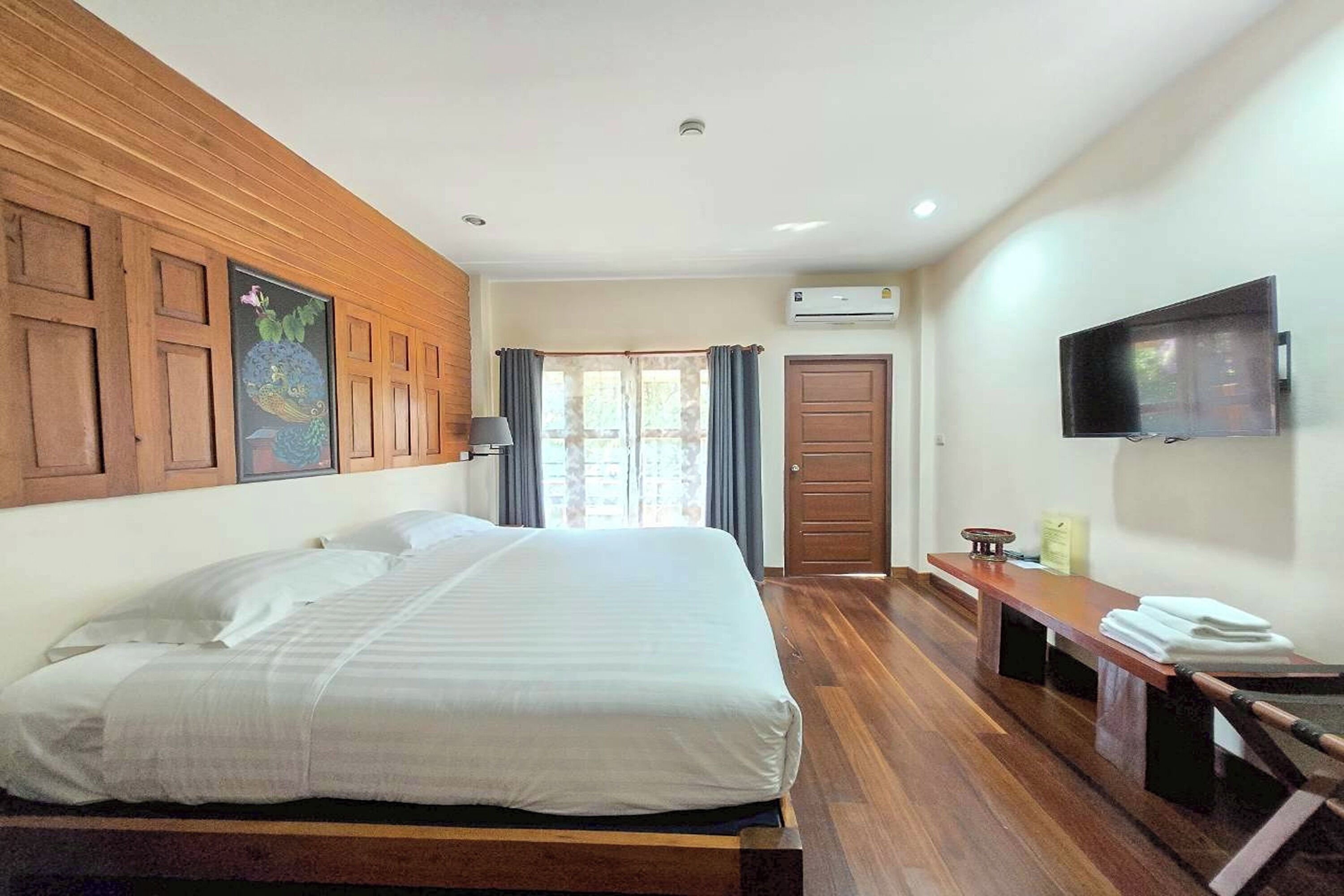 A hotel room with a large bed, wooden paneling on the walls, a flat-screen TV, a desk with a chair, and a window with curtains.