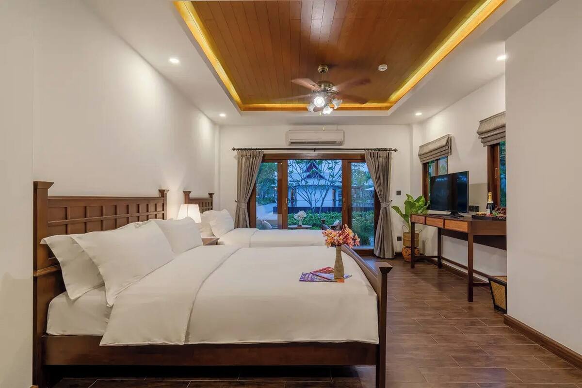 A hotel room with two beds, a desk with a TV, and a view of a traditional building outside.