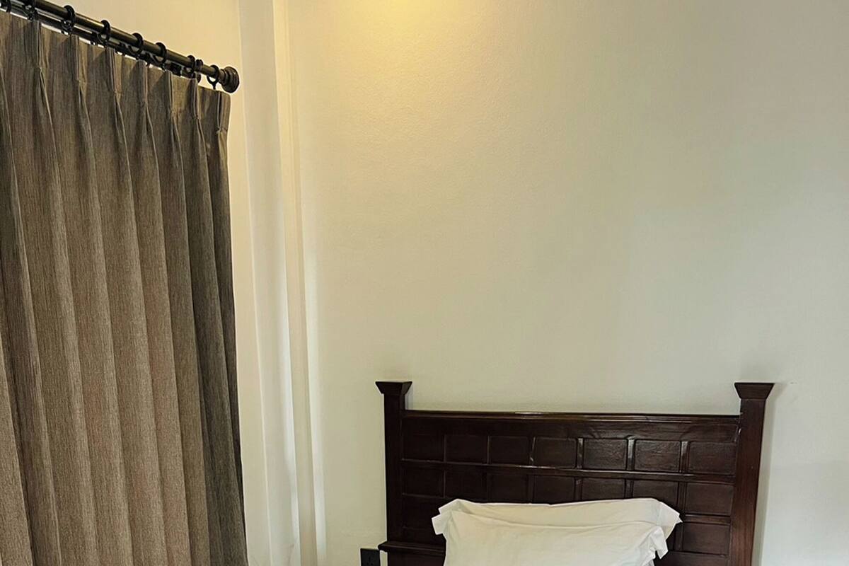 A neatly made bed with a wooden headboard, a white pillow, and a folded white towel on the footboard.