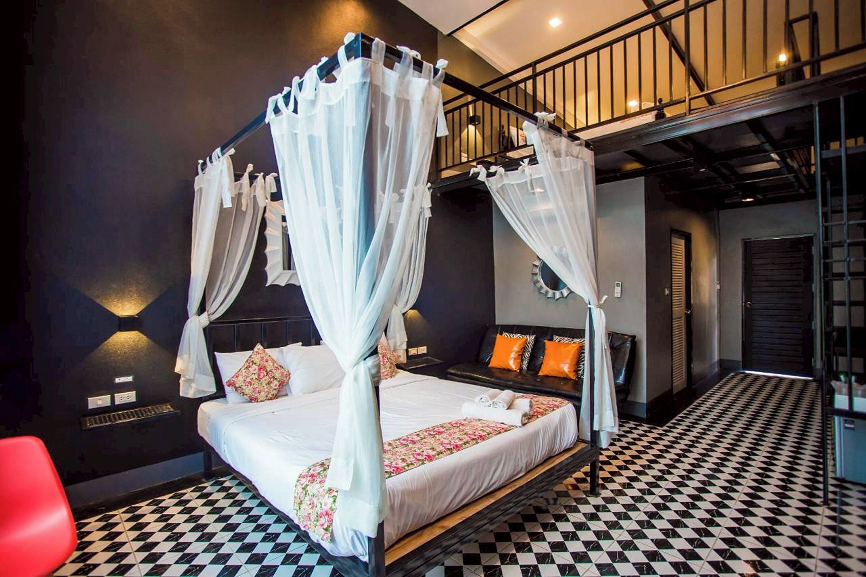 A four-poster canopy bed with a checkered floor, a red chair, and a staircase in the background.