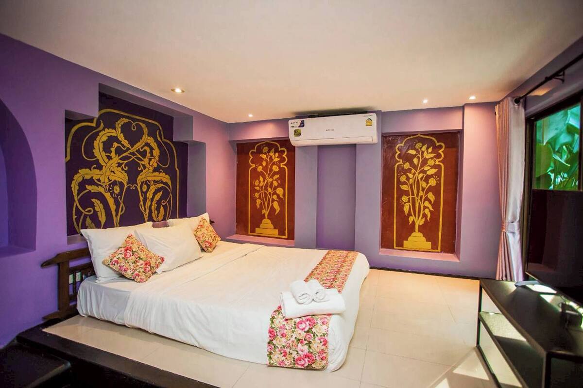 A bedroom with a bed, pillows, a bedside table, and a wall-mounted air conditioner.