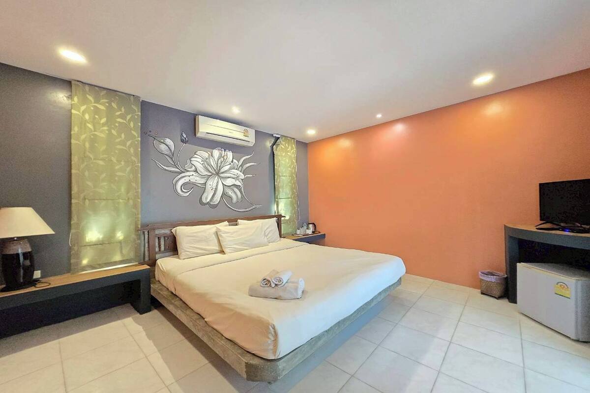 A hotel room with a large bed, a nightstand, a lamp, a TV, and a wall-mounted air conditioner.