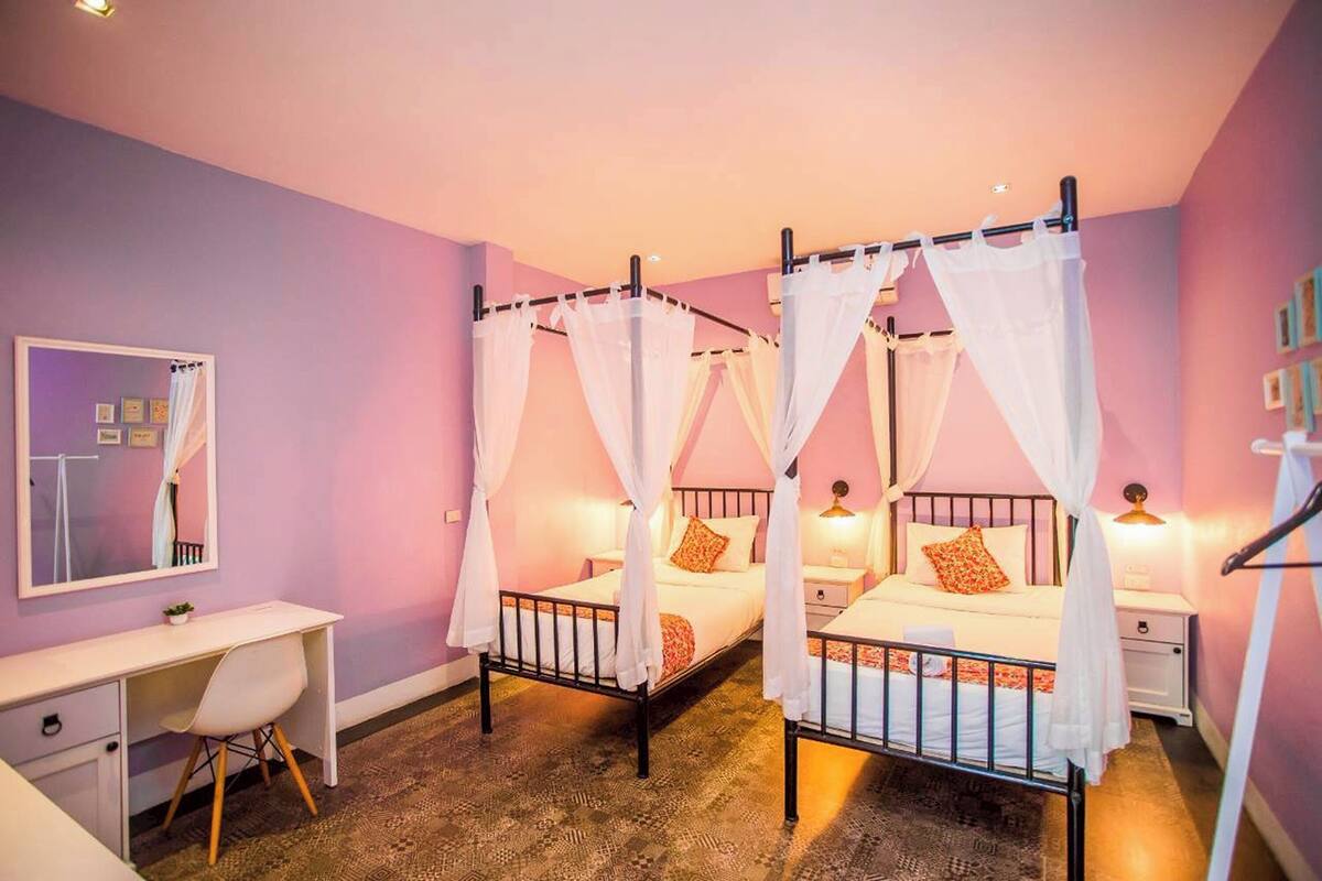 A bedroom with two beds, each with a canopy, a desk, and a chair.