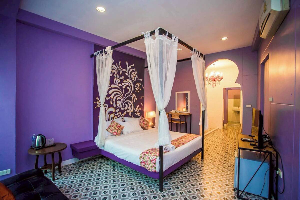 A bedroom with a four-poster bed, a small table, a chair, and a desk with a computer.