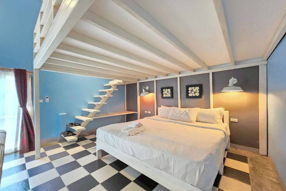 A bedroom with a checkered floor, a bed with white linens, a white staircase, and wall-mounted lamps.