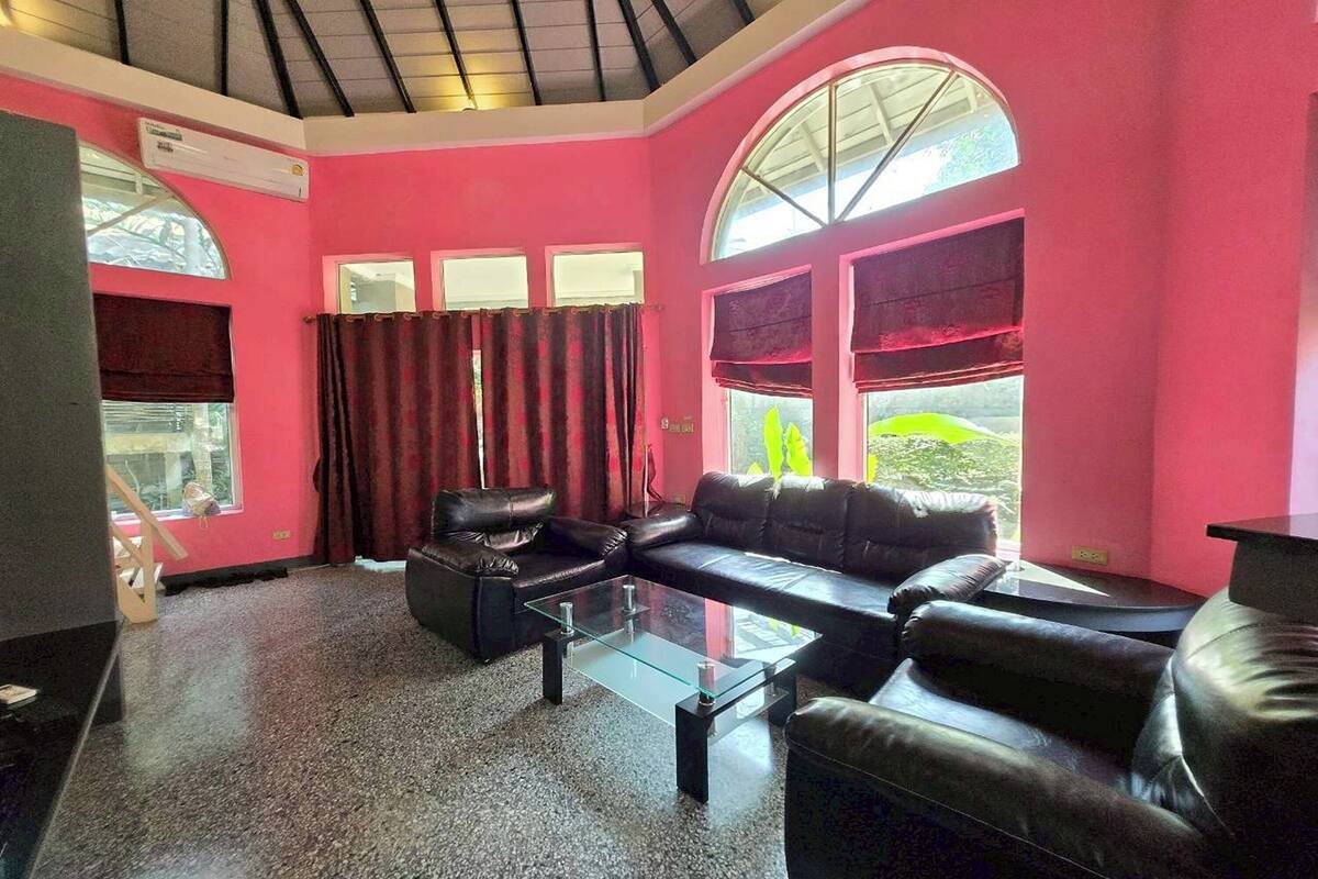 A living room with a glass coffee table, black leather sofa, and red curtains.