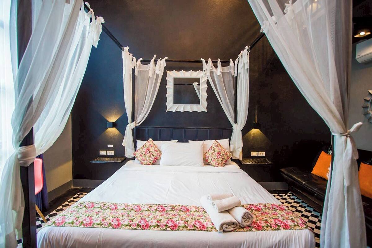 A four-poster canopy bed with white linens and floral bedding, two bedside lamps, and a checkered floor.