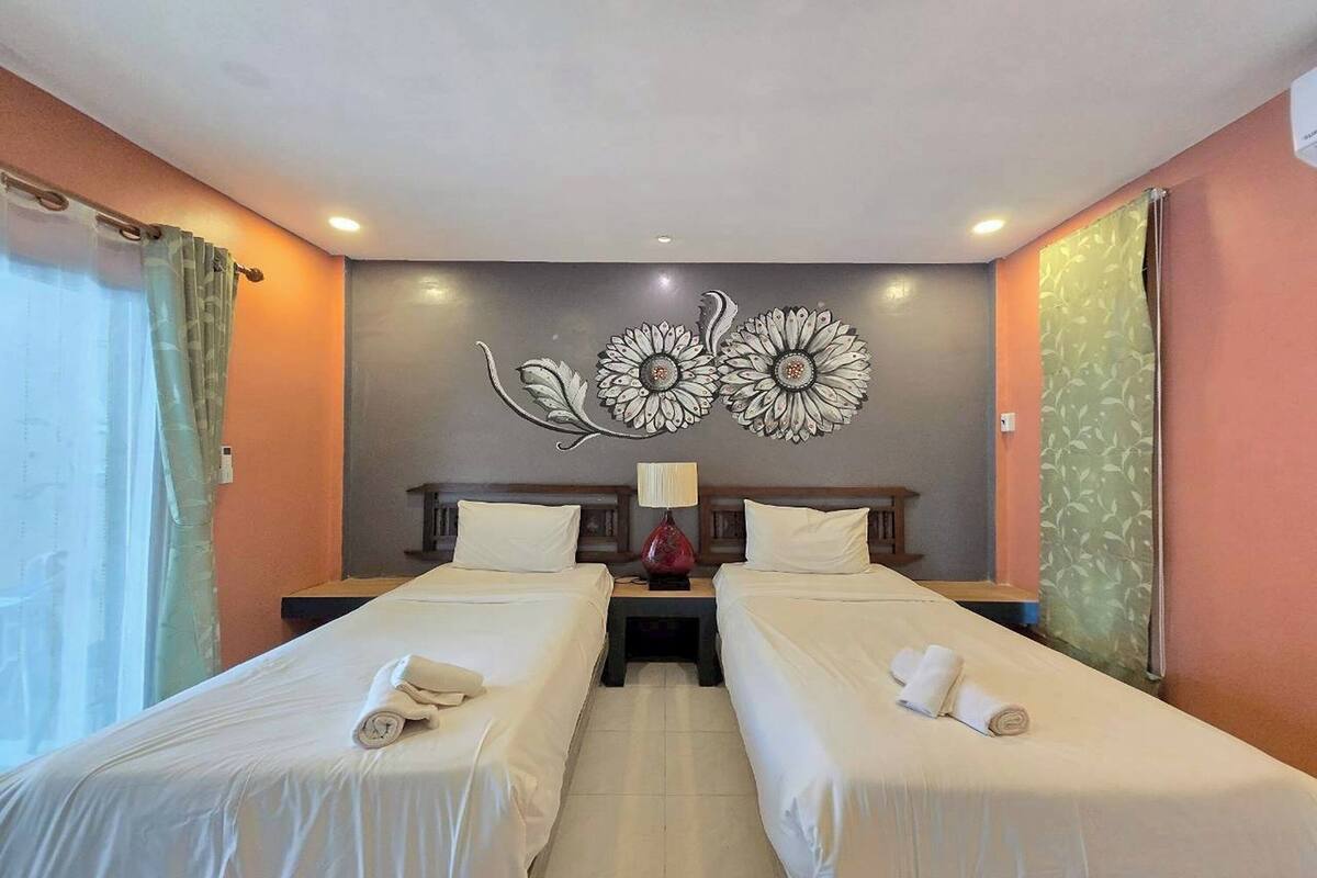 A hotel room with two single beds, a nightstand with a lamp, and a decorative wall art piece.