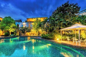 A swimming pool with a sunken seating area, surrounded by lush greenery and modern buildings. - Paeva Luxury By Nakra Functionality (Bang Sao Thong)
