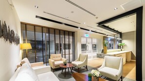 Eine moderne Hotelhalle mit einer Couch, Sesseln, einem Couchtisch und einer Küche im Hintergrund.