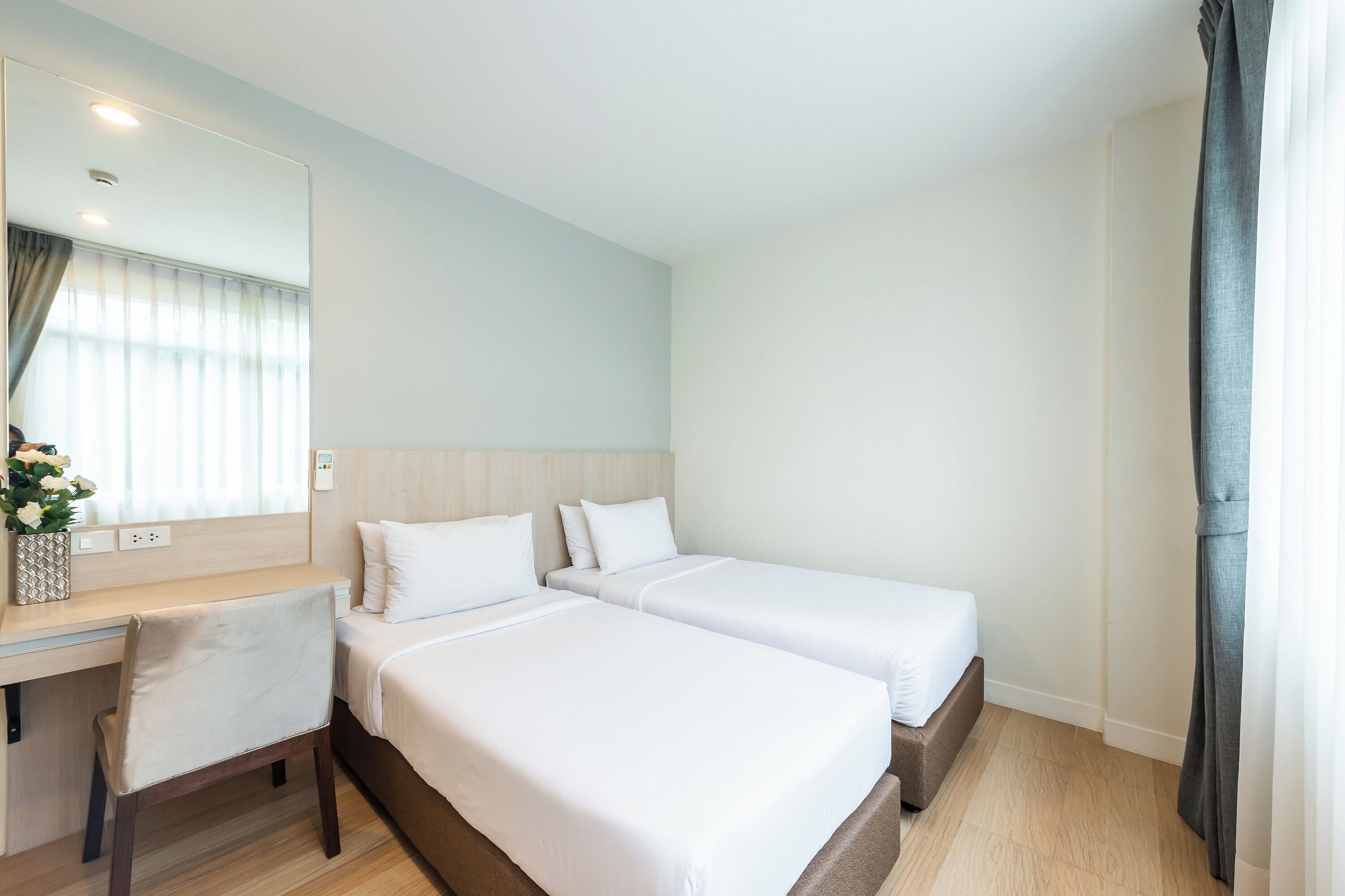 Ein Hotelzimmer mit zwei Betten, einem Schreibtisch, einem Stuhl, einem Spiegel und einem Fenster mit Vorhängen.