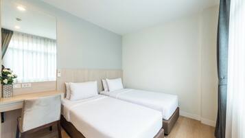 Ein Hotelzimmer mit zwei Betten, einem Schreibtisch, einem Stuhl, einem Spiegel und einem Fenster mit Vorhängen.