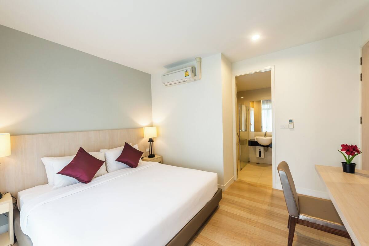 A hotel room with a bed, bedside lamps, a desk, and a bathroom visible through an open door.