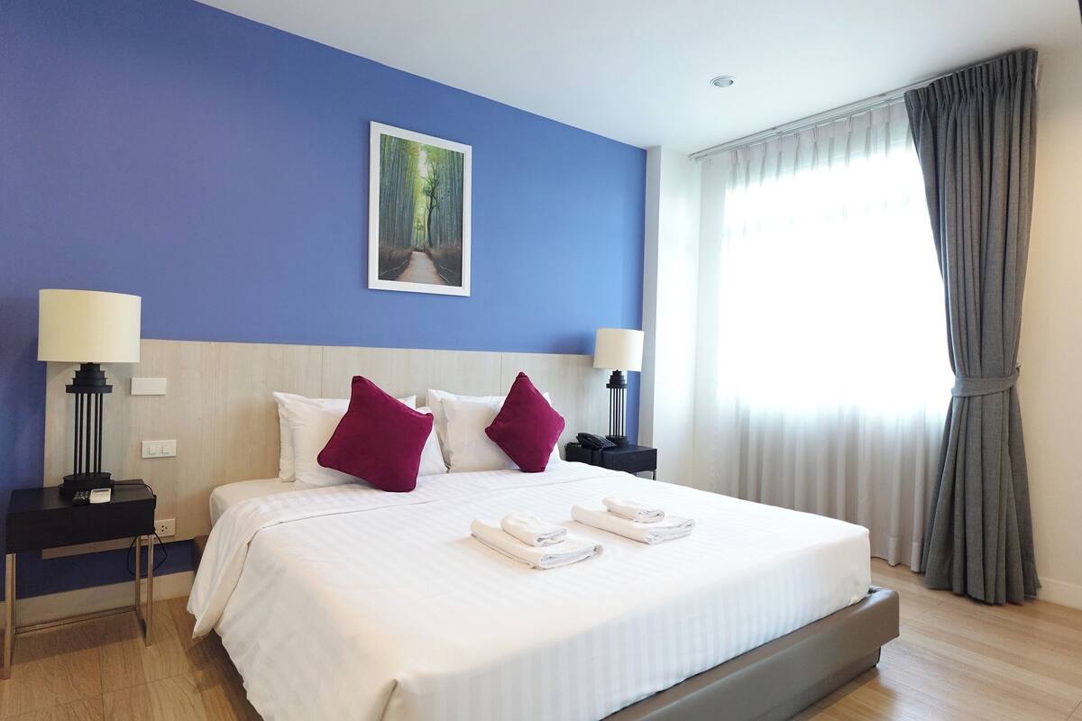 A hotel room with a large bed, two nightstands, a painting on the wall, and a window with curtains.