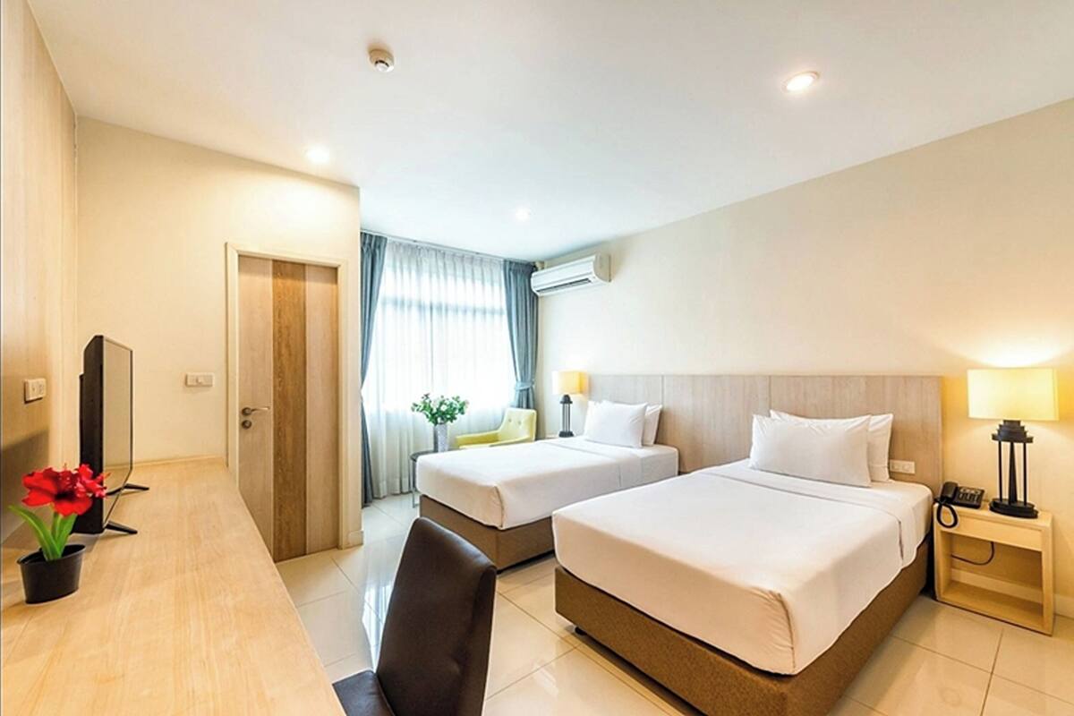 A hotel room with two beds, a desk, a chair, a TV, and a window with curtains.