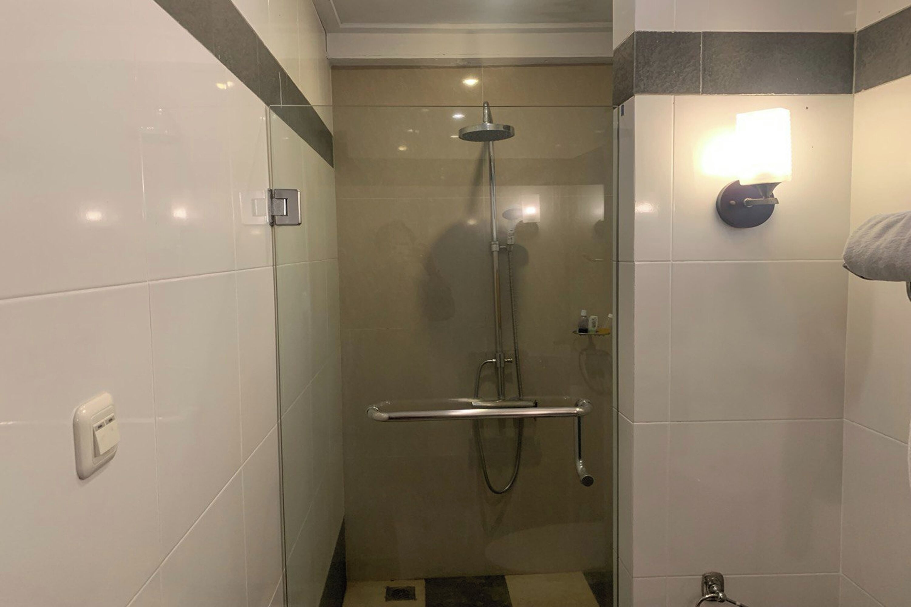 A shower with a handheld showerhead, a glass door, and a wall-mounted light fixture.