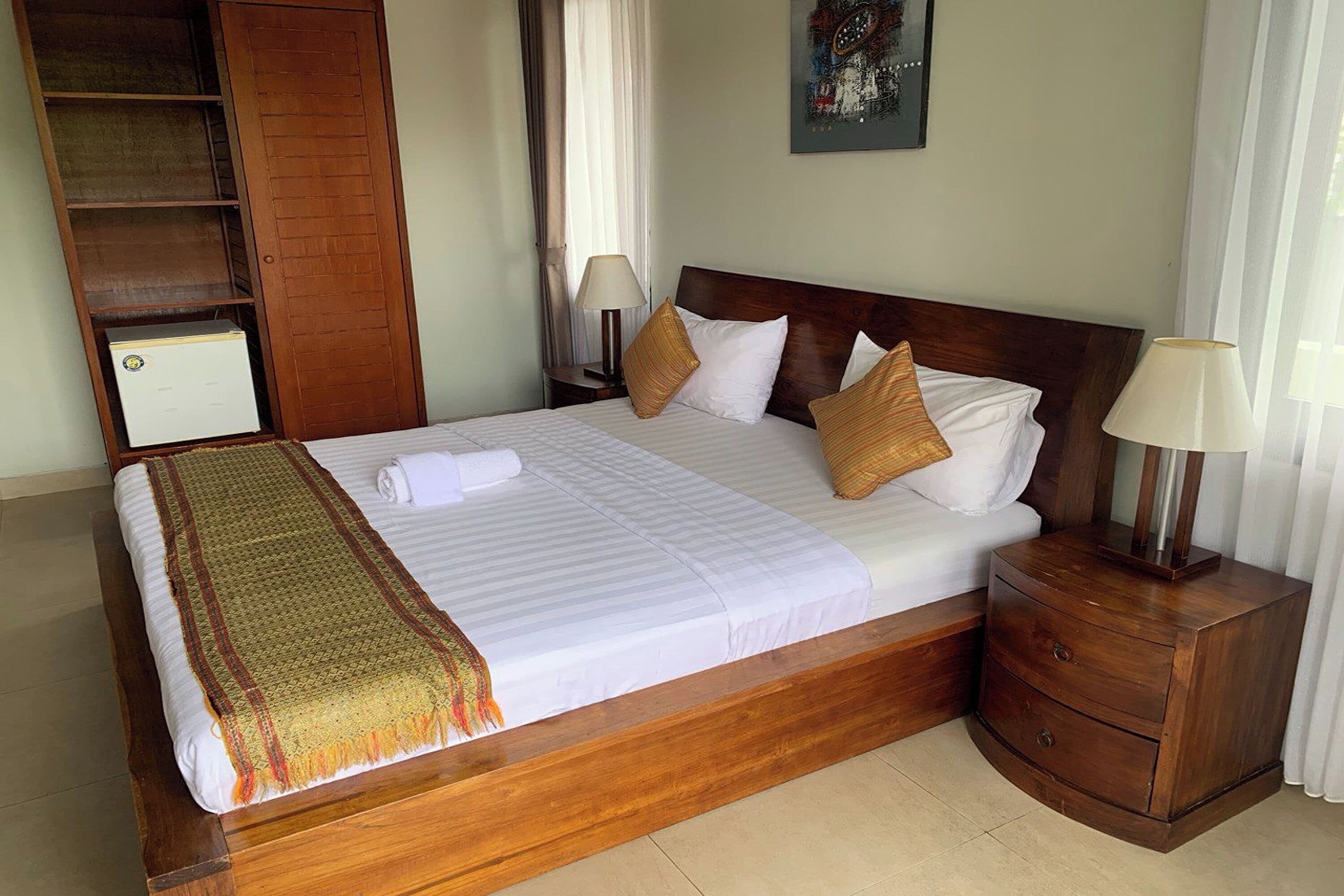 A neatly made bed with a wooden headboard, a bedside table with a lamp, and a wardrobe.