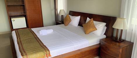 A neatly made bed with a wooden headboard, a bedside table with a lamp, and a wardrobe.