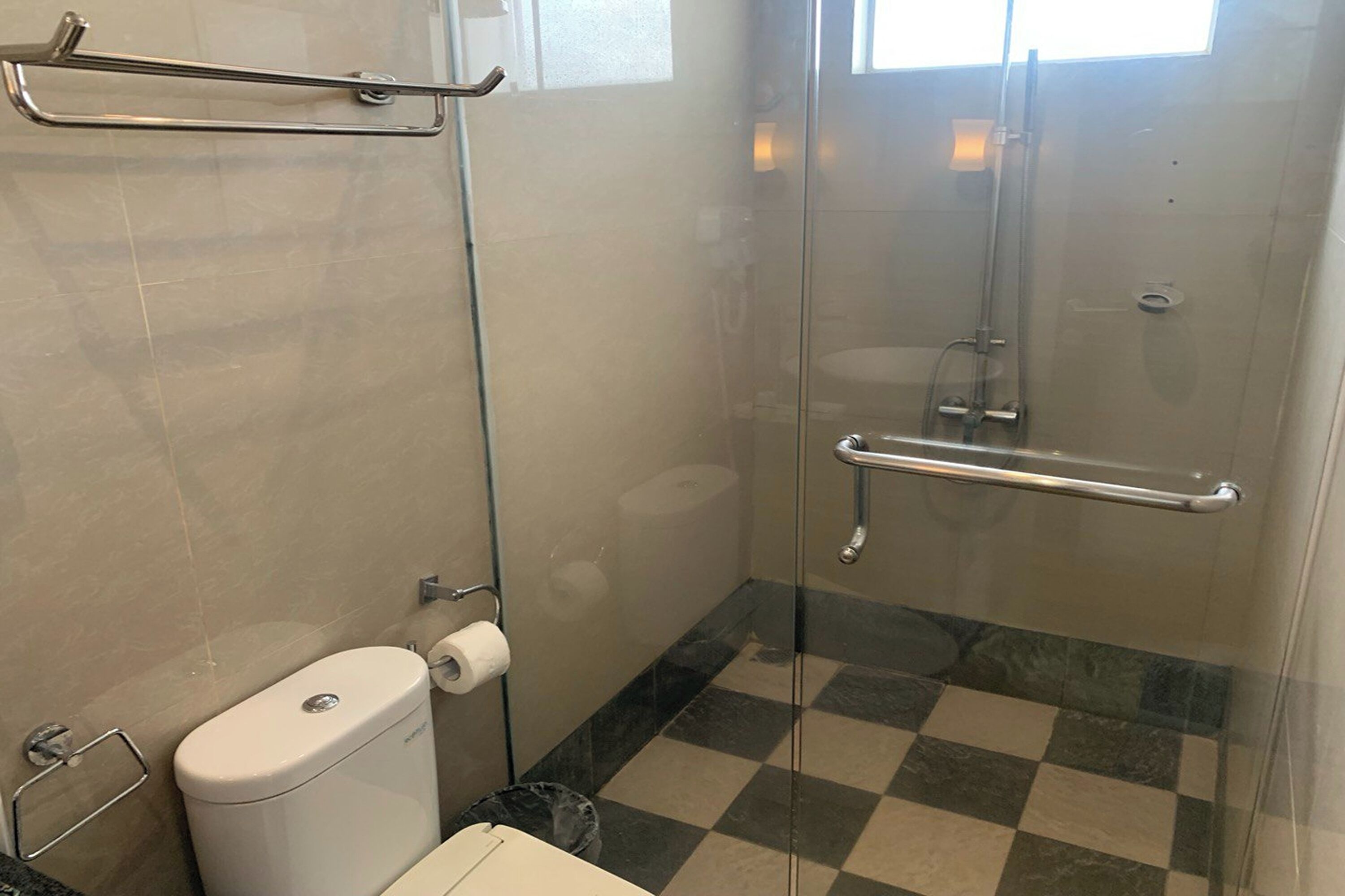 Et badeværelse med glasbrusekabine, toilet og et skakternet gulv.