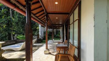 A covered outdoor seating area with wooden furniture and a stone pathway leading to a water feature.