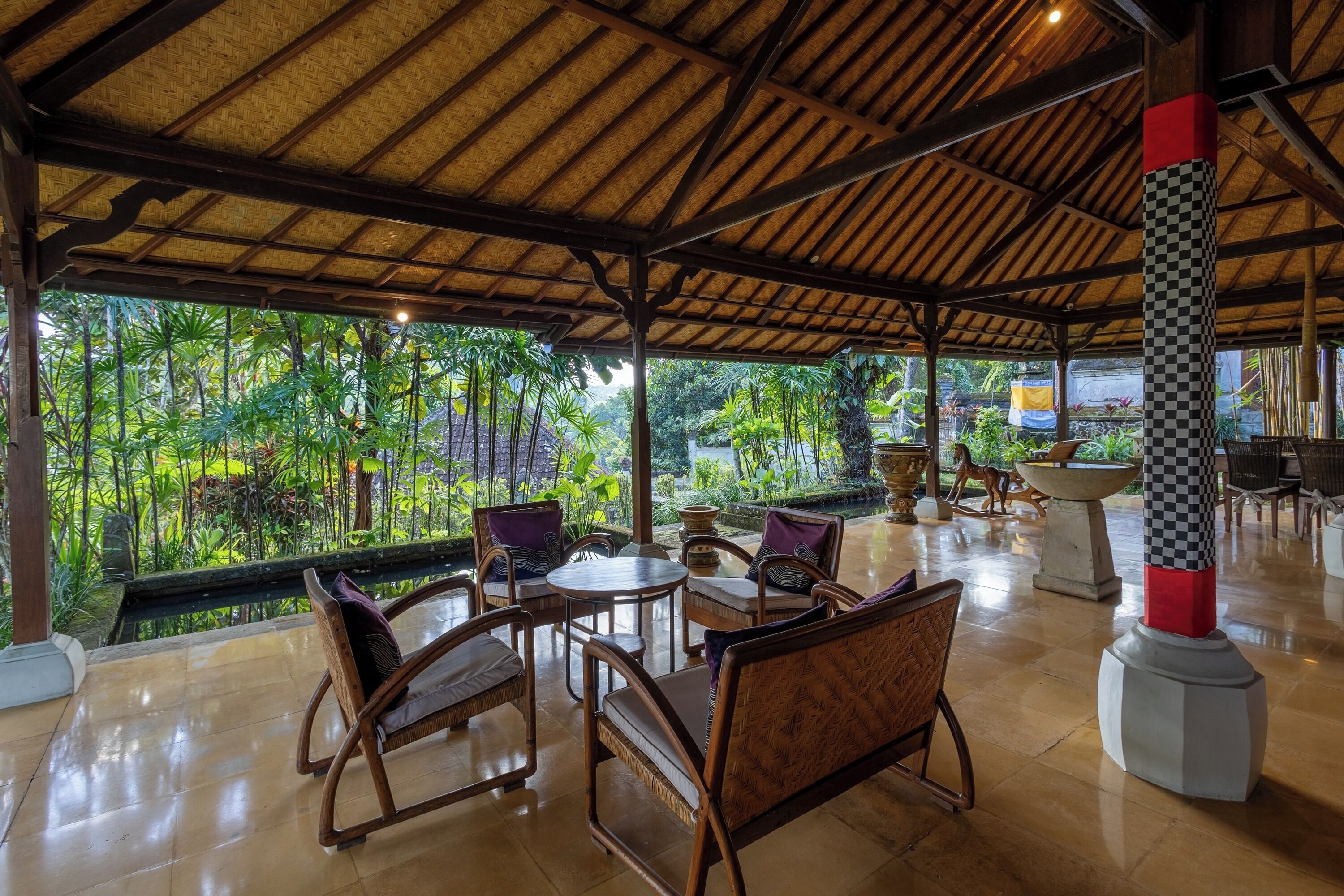 Un espacio interior con techo de paja, mobiliario de madera y vistas a exuberante follaje.