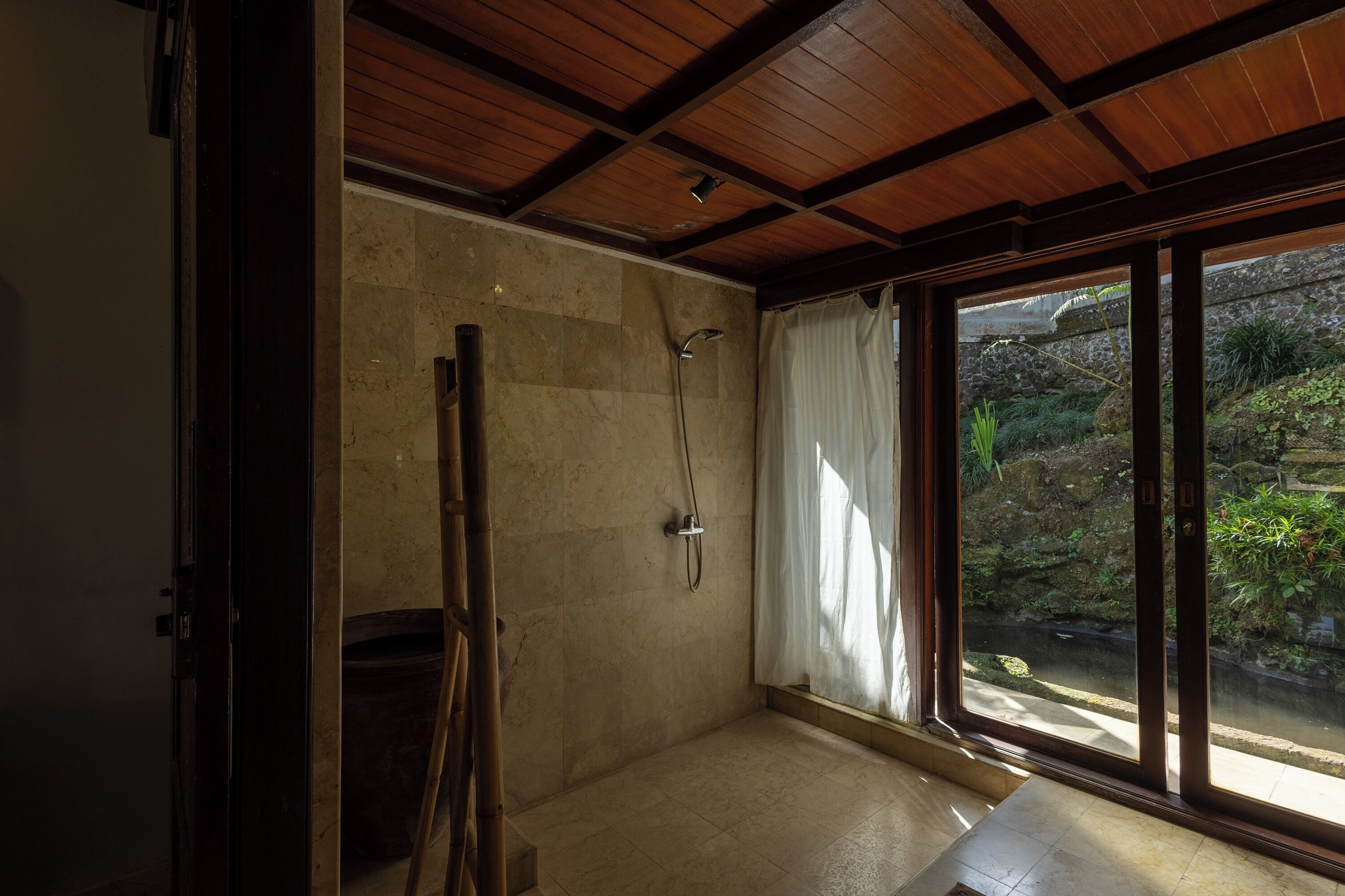 Un baño con ducha, una puerta de madera y vistas a un jardín rocoso a través de un amplio ventanal.