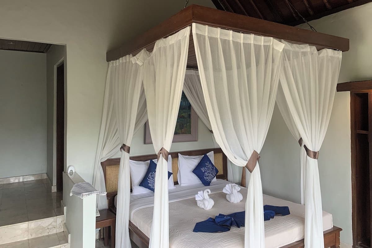 A four-poster canopy bed with white linens, pillows with blue and white patterns, and a wooden headboard.