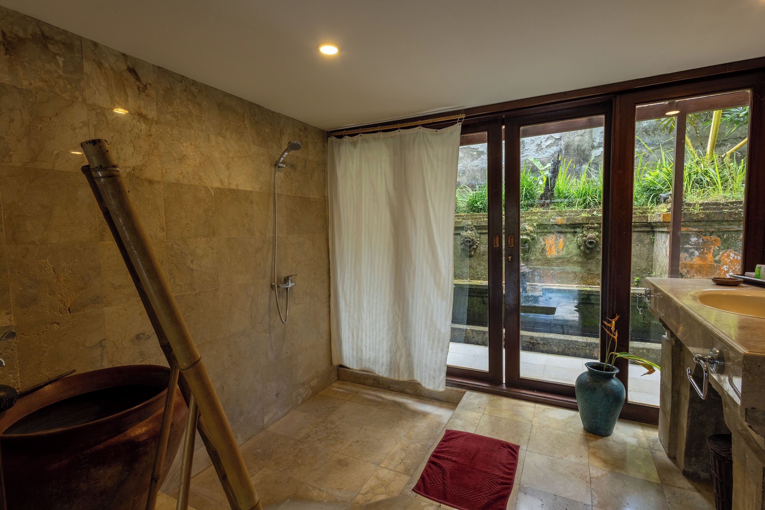 Ein Badezimmer mit Dusche, Waschbecken und Blick auf einen Garten durch eine Glastür.